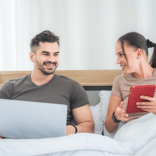couple in bed with laptops and a tablet discussing how to budget for your first home