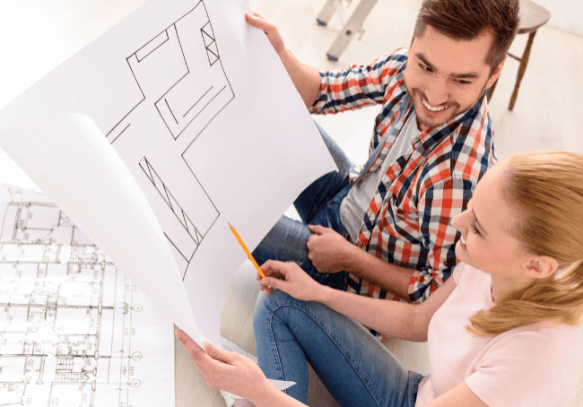 Two people sitting on the floor looking at their house plans. They're building their first home