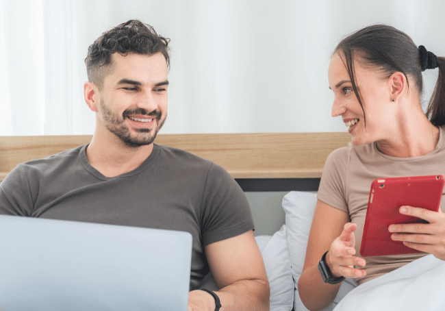 couple in bed with laptops and a tablet discussing how to budget for your first home